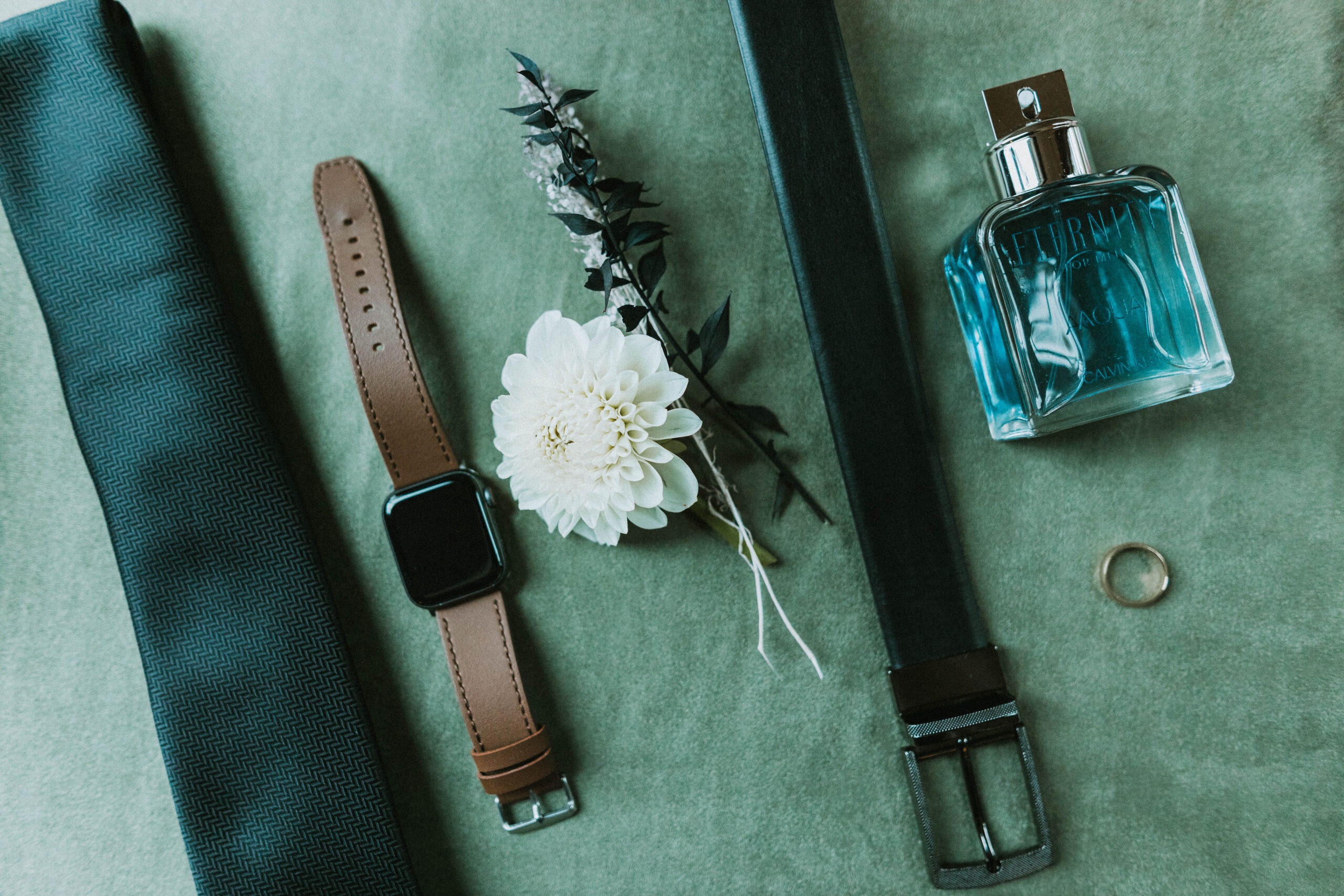 Wedding Day Flat Lay featuring a tie, watch, floral arrangement, belt, and cologne fo